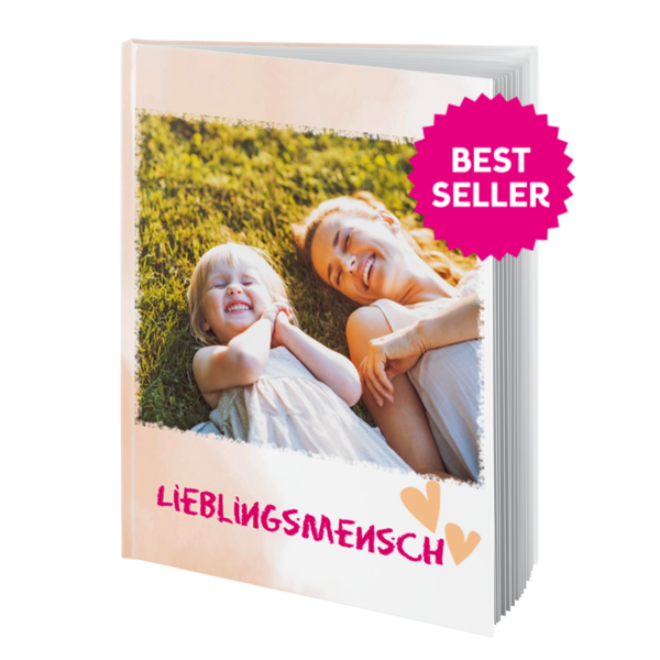 Auf dem Cover eines Fotobuchs sind eine Mutter und ihre Tochter zu sehen, die lachend im Gras liegen.